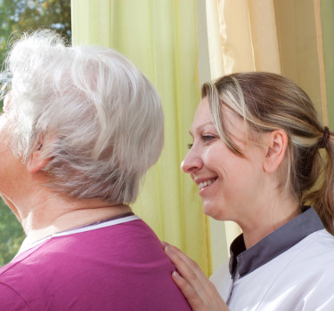 female nurse and elderly woman standing at the window